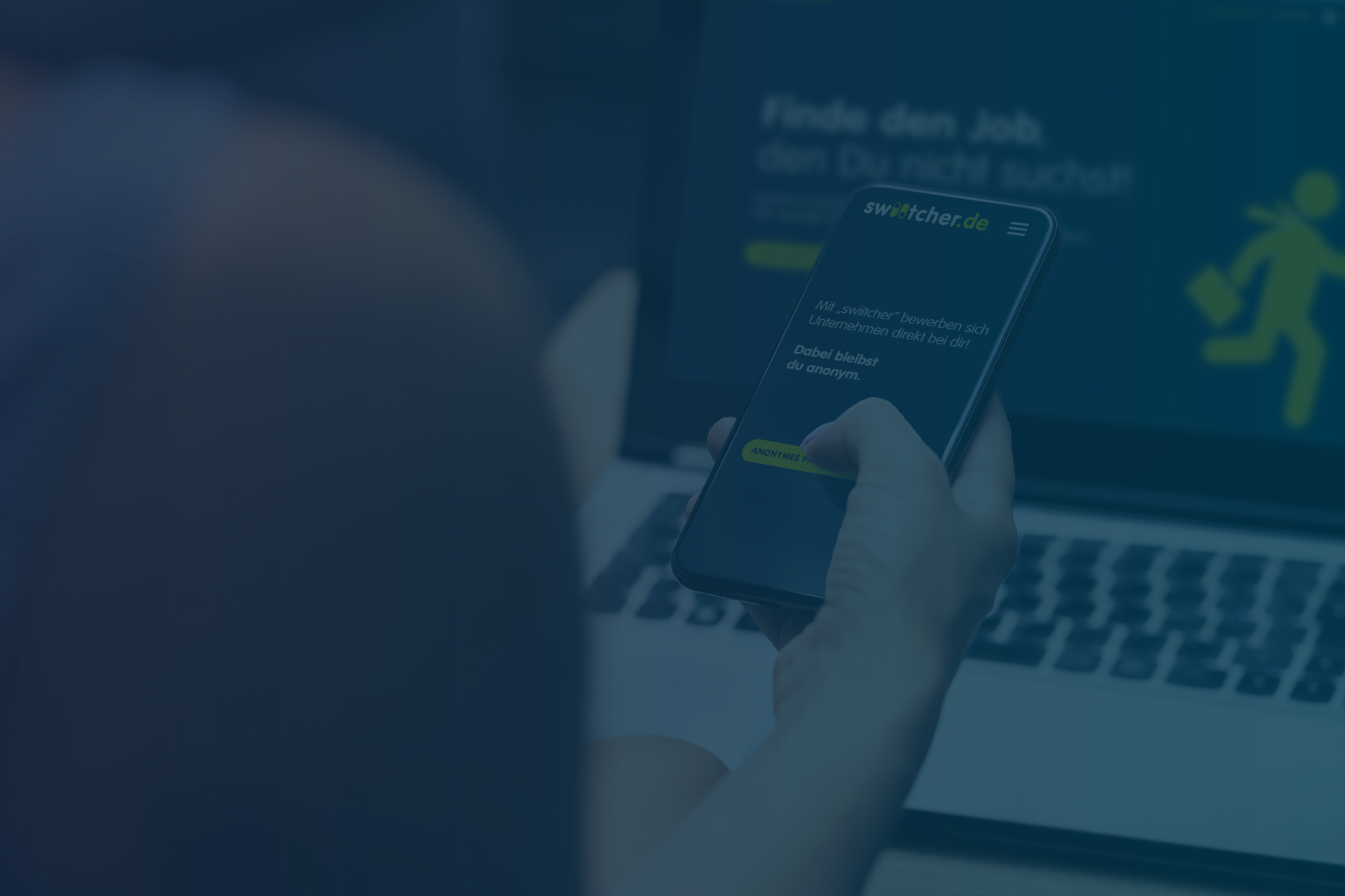 Sicht über die rechte Schulter einer Person auf ein Smartphone, das in der Hand gehalten wird. Auf dem Bildschirm des Smartphones ist die swiitcher-Startseite zu sehen. Die Person tippt auf den Button "Anonymes Profil erstellen"